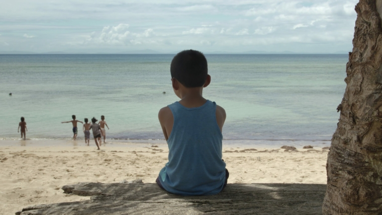 Nonoy sitzt am Strand und schaut den anderen Kindern beim Spielen zu.