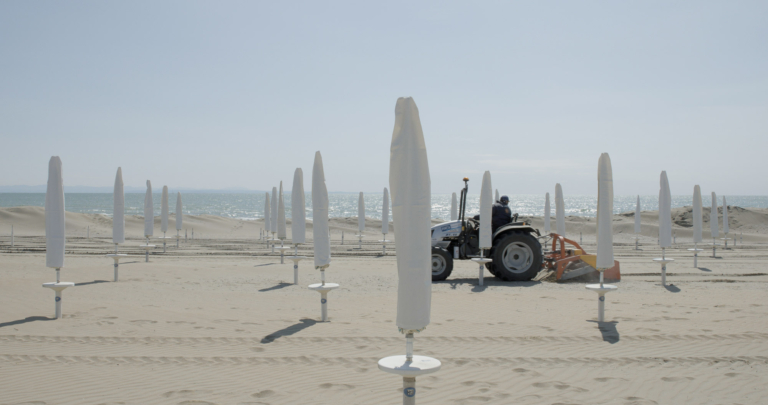 Ein Traktor am Strand zwischen Sonnenschirmen bei Saisonstart des Dokumentarfilms Vista Mare