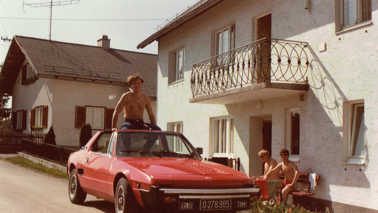 Ein Mann mit nacktem Oberkörper sitzt am Dach eines roten Cabrios im Serienpitch Schneewalzer von Patrick Neubäck